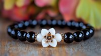 Elegant black onyx beaded bracelet with white flower accent and copper details on rustic wooden surface, suitable for jewelry photography and fashion accessories.