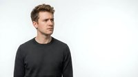 Young adult male with light skin tone and brown hair wearing dark gray crew neck sweatshirt, looking to the side against white background for portrait and apparel design use.