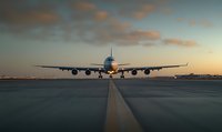 Commercial passenger airplane on runway during sunset with dramatic orange clouds, front view perspective showing aircraft ready for takeoff or landing.