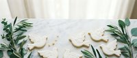 Homemade sugar cookies shaped like dinosaurs decorated with white icing on marble surface with eucalyptus leaves for baking and dessert projects.