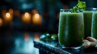 Fresh green smoothie with ginger root and herbs garnish on dark moody background with glowing candles, healthy detox drink served in tall glass.