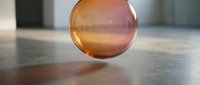 Transparent amber glass sphere casting warm light and shadow on concrete surface, suitable for abstract backgrounds and design projects.