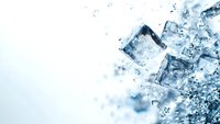 Ice cubes splashing in water with droplets and bubbles creating refreshing cool effect on light blue background.