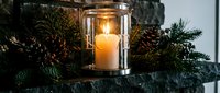 Glowing candle lantern with love inscription on stone mantel, surrounded by pine branches and cones, creating a cozy winter holiday atmosphere.