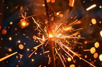 Glowing sparkler with bright golden sparks and bokeh lights bursting against dark background, suitable for celebrations, New Year, fireworks, and festive event designs.