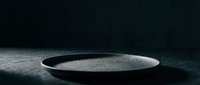 Empty black ceramic bowl with fine sand texture on dark surface, minimalist still life composition for design and editorial use.