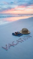 Vacation written in sand on a tropical beach at sunset with straw hat and flip flops, evoking summer travel and holiday relaxation.