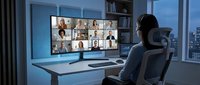 Professional businessman attending virtual team meeting on dual monitors in modern office workspace with city view at dusk.