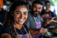 Smiling Hispanic female barista in colorful apron with curly hair at coffee shop counter, coworkers preparing food in background. Natural lighting creates warm ambiance.