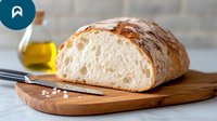 Fresh crusty artisan bread loaf sliced on wooden cutting board with olive oil and sea salt, showing airy crumb texture and crispy crust. For food photography.
