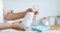 Man with medium skin tone holding white cylindrical bottle with dispenser pump in kitchen setting, suitable for health, beauty, cleaning product marketing and packaging mockups.
