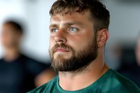 Confident Caucasian male athlete in green jersey with full beard and determined expression looking ahead during sports event or training session.