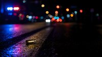 Blurred night city street with colorful bokeh lights reflecting on wet asphalt pavement creating atmospheric urban scene for backgrounds and design projects.