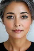 Close-up portrait of mature Asian woman with silver gray hair, natural makeup, and warm brown eyes against light background, showing graceful aging and confidence.