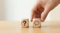 Hand placing wooden cube with speech bubble next to question mark block on desk for communication and problem-solving concepts in business.