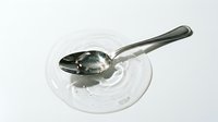 Silver metal spoon resting on clear glass plate with water droplets creating elegant reflections on white background for kitchen and dining concepts.
