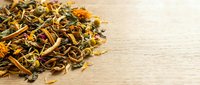Dried herbal tea blend with flowers, leaves and botanicals scattered on natural wooden surface for wellness and beverage preparation.