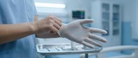 Healthcare professional putting on protective latex gloves in sterile medical environment preparing for patient examination or surgical procedure.