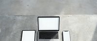 Modern workspace setup with laptop, tablet and smartphone displaying blank white screens on concrete surface for digital mockup and presentation needs.