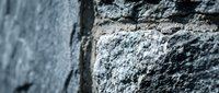 Close-up view of rough textured gray stone surface with natural cracks and weathered details for construction and architectural backgrounds.