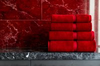 Stack of folded red cotton towels on gray marble surface against red marble wall, luxury bathroom interior design concept.