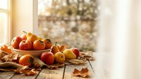 Autumn harvest display with fresh apples and pumpkins on rustic wooden table surrounded by golden fall leaves in warm sunlight for seasonal decoration.