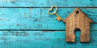 Wooden house shape and golden key on turquoise blue rustic wooden background. Real estate concept, house purchase, mortgage and property investment.