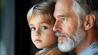 Emotional portrait of mature bearded man with gray hair and young boy looking away thoughtfully against dark background. Family bonding moment captured in natural light.