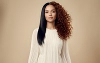 Young mixed-race woman with half straight half curly hairstyle in cream sweater on beige background for beauty and fashion concepts.