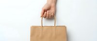Hand holding brown kraft paper shopping bag against white background for eco-friendly retail and sustainable packaging concepts.