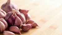 Fresh garlic cloves with papery skin scattered on wooden surface, suitable for culinary, food styling, and cooking-related projects.