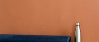 Stainless steel water bottle and rolled blue yoga mat on terracotta background for fitness, wellness and healthy lifestyle design projects.