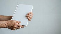 Mature man with weathered hands holding blank white book or magazine against neutral background, suitable for publishing, education, and business marketing materials.