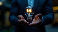 Glowing vintage filament light bulb floating between male hands in dark suit, dramatic lighting creates mysterious atmosphere for business innovation concept.