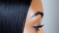 Close up portrait of young Asian woman with flawless skin, long black straight hair, and professional makeup showing eye and eyebrow detail against light background.