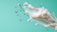 Dynamic white milk splash with droplets against mint green background, capturing liquid motion and dairy freshness in studio lighting conditions.