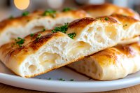 Golden baked bread rolls filled with melted cheese, garnished with fresh herbs on white plate. Perfect for bakery menus, comfort food blogs, and culinary content.