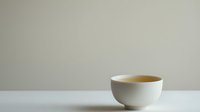 White ceramic bowl with hot tea on minimalist white table against neutral wall background, emphasizing simplicity and zen atmosphere in modern interior setting.