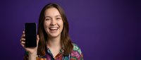 Happy young Caucasian woman with long brown hair displaying smartphone screen on purple background for mobile app marketing and technology advertising.