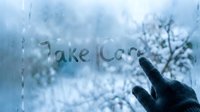 Take Care written on a foggy winter window by a gloved hand, with snowy trees visible through the glass in cool blue tones.