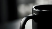 Black coffee mug close-up with shallow depth of field creating moody atmosphere for morning beverage concepts and cafe marketing materials.