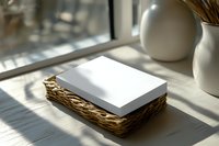 Blank white paper stack in woven basket near window with natural sunlight and shadow patterns creating minimalist composition for stationery mockup.
