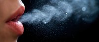 Close-up of human mouth exhaling visible breath vapor with water droplets against dark background for health and respiratory concepts.