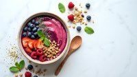 Healthy acai smoothie bowl topped with fresh berries, granola and mint leaves on marble background for breakfast nutrition and wellness lifestyle.