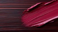 Red lipstick smear with creamy texture creating elegant makeup stroke on dark background for cosmetic and beauty product advertising campaigns.