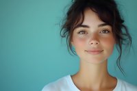 Young woman with natural makeup and messy bun hairstyle wearing white t-shirt smiling against turquoise background, fresh glowing skin and gentle expression.