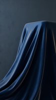 Elegant navy silk fabric draped over geometric form against textured gray background, showcasing luxurious material flow and sophisticated styling for fashion, luxury goods, and interior design projects.
