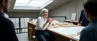 Middle Eastern female architect in hijab presenting building plans to colleagues in modern office meeting room during professional consultation.