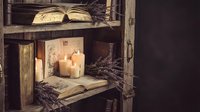 Cozy rustic wooden shelf with open books, burning candles and dried lavender creating warm atmospheric reading nook for home decor and relaxation.
