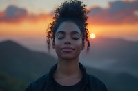 Young African American woman with natural curly hair in high bun smiling peacefully with eyes closed against dramatic mountain sunset sky background.